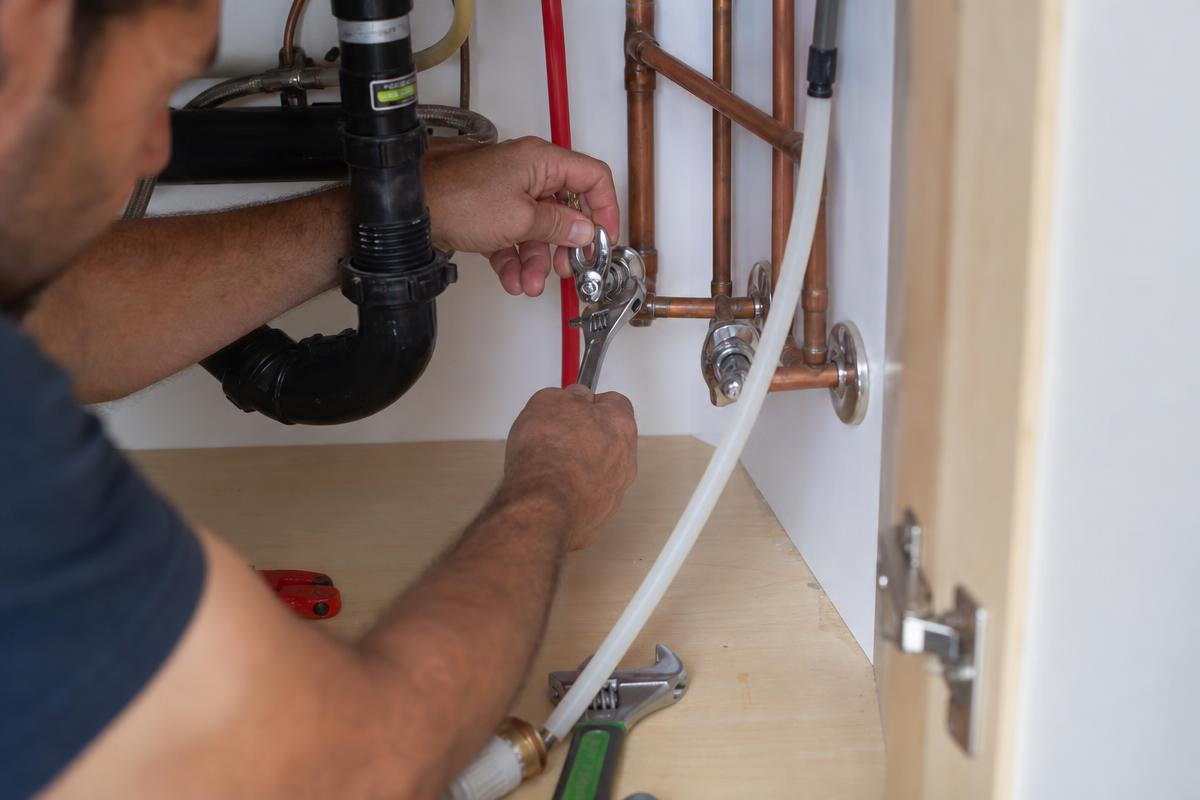 Plomero instalando tuberías de cobre y PEX bajo un fregadero de cocina